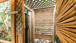 Una estructura de madera con una puerta de bambú y un cartel que indica zona de duchas.