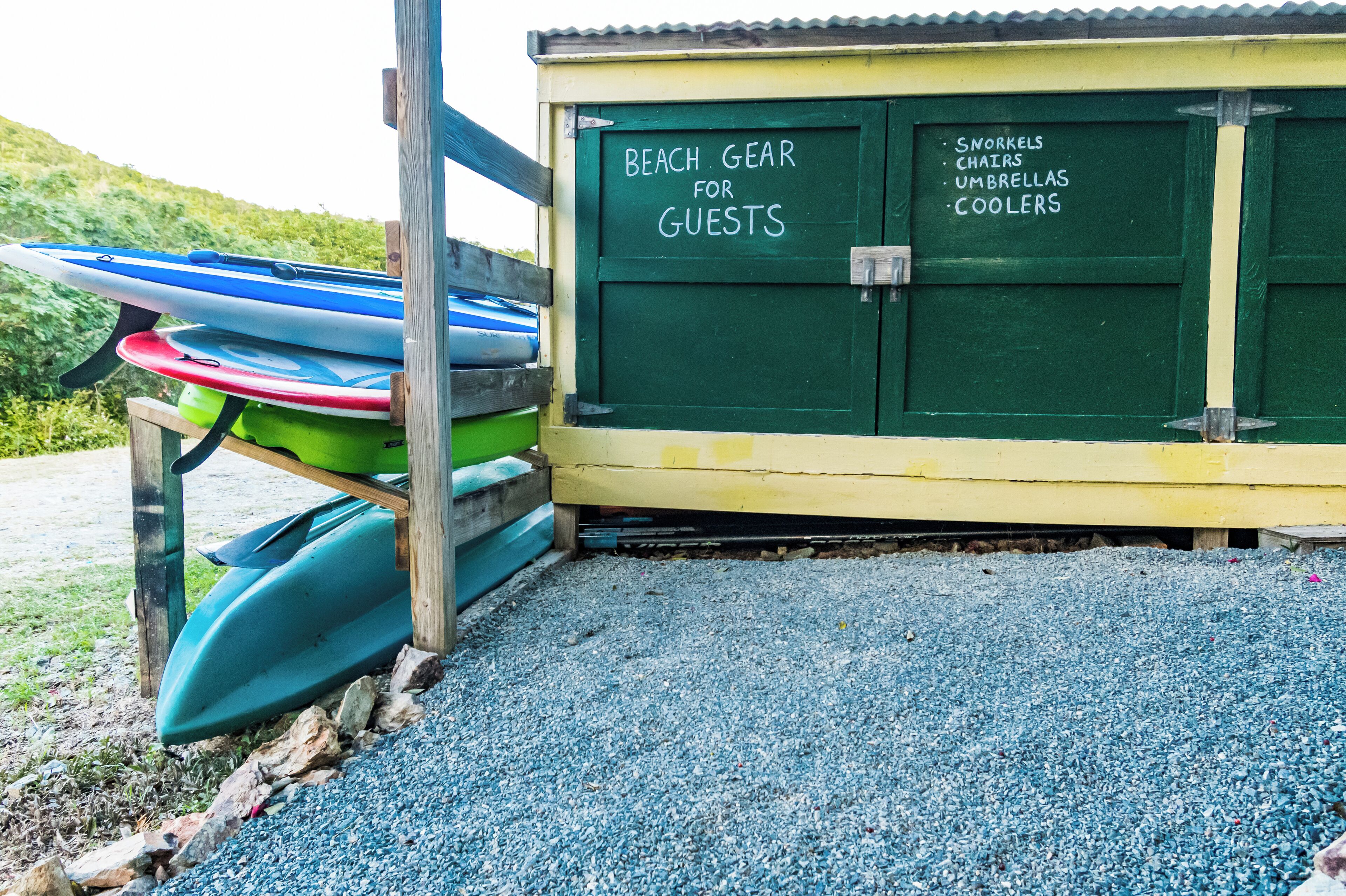 Un área de almacenamiento para equipo de playa con tablas de surf y un cartel que enumera artículos como snorkels, sillas, sombrillas y hieleras.