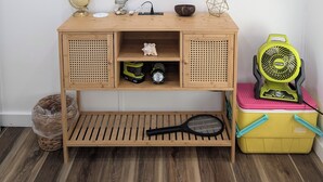 Un mueble bajo de madera para televisor con un televisor de pantalla plana montado encima, un globo terráqueo, un reloj pequeño, un cuenco decorativo y un ventilador.