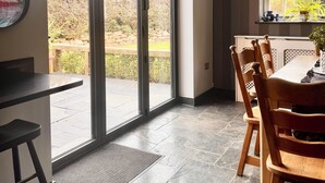 Un comedor moderno con una mesa grande y sillas, una encimera de cocina y vistas al exterior a través de puertas correderas amplias.