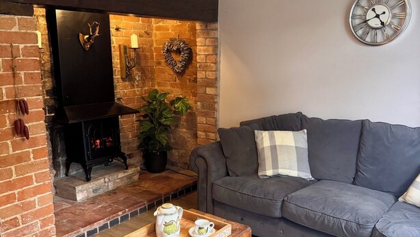 Una sala de estar acogedora con chimenea, un sofá gris, una mesa de centro de madera con juego de té y un reloj en la pared.