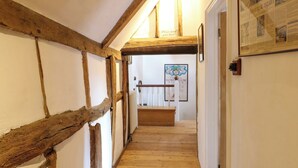 A narrow hallway with exposed wooden beams, a wooden staircase, and a framed poster on the wall. - Bank House (Norwich)