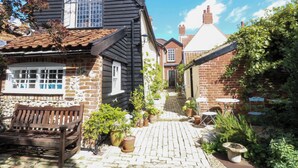 A traditional brick house with a tiled roof, a wooden bench, and potted plants in the garden area. - Bank House (Norwich)