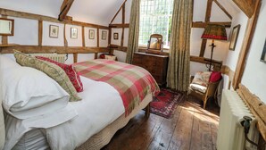 A bedroom with a large bed, wooden beams, a dresser, a chair, and a window with curtains. - Bank House (Norwich)