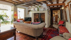 A cozy living room with a fireplace, wooden beams, and a television. - Bank House (Norwich)