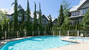 Une piscine entourée d’une terrasse, d’arbres et d’un bâtiment au style architectural particulier.