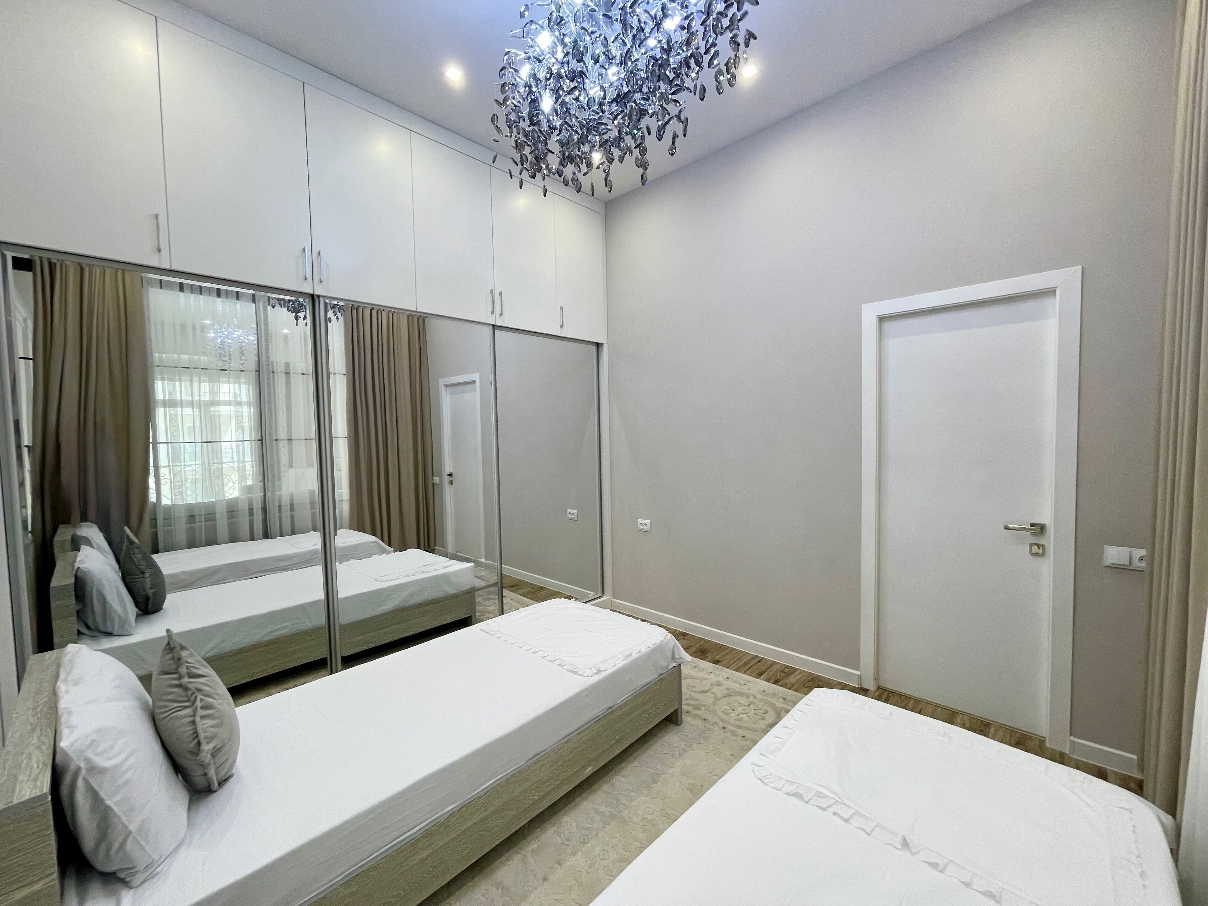 A modern bedroom with a large bed, a smaller bed, a walk-in closet, and a glass partition.