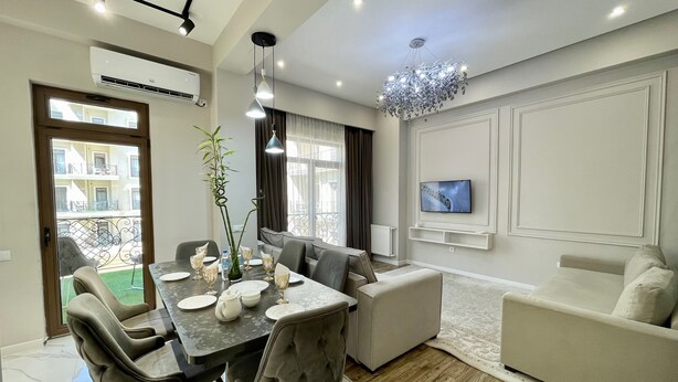 A modern living room with a dining area, a sofa, a TV mounted on the wall, and a balcony visible through the door. - Boulevard steak house (Tashkent)