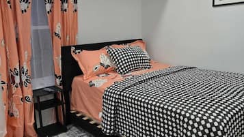 A bedroom with a bed, a nightstand, a window with curtains, a rug, and a framed picture on the wall.