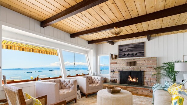 A cozy living room with a fireplace, comfortable seating, and large windows overlooking the sea.