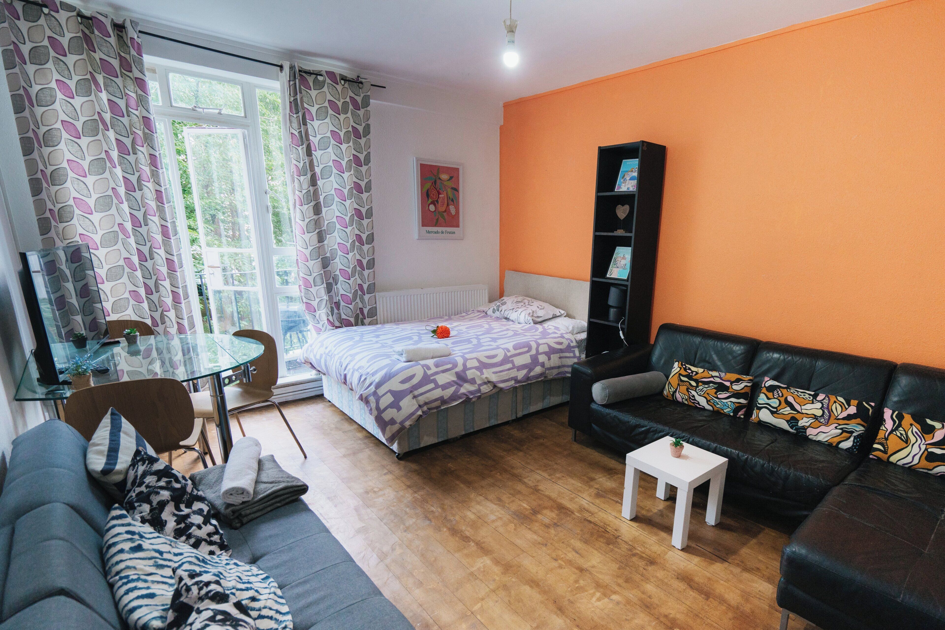 Una habitación moderna con una cama, un sofá, una mesita, una estantería y una mesa de vidrio con sillas.