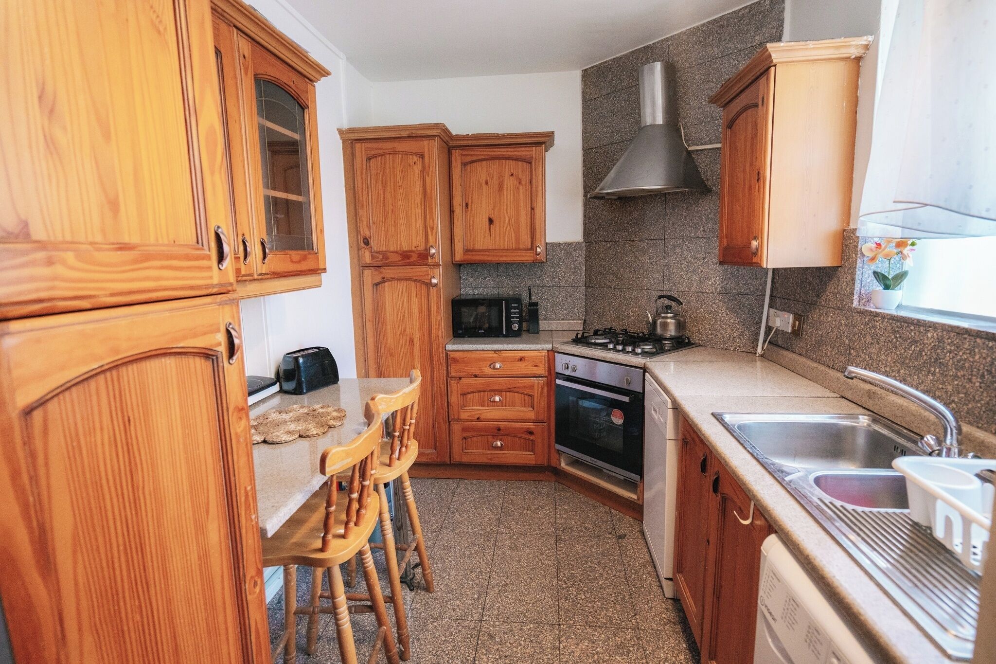 Eine kleine Küche mit Holdekor, einer Mikrowelle, einem Backofen, einem Spülbecken und einem Fenster mit einer Pflanze.