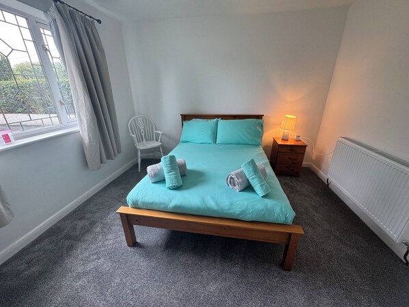 Un dormitorio con una cama, una silla, una mesita de noche y una ventana con cortinas.