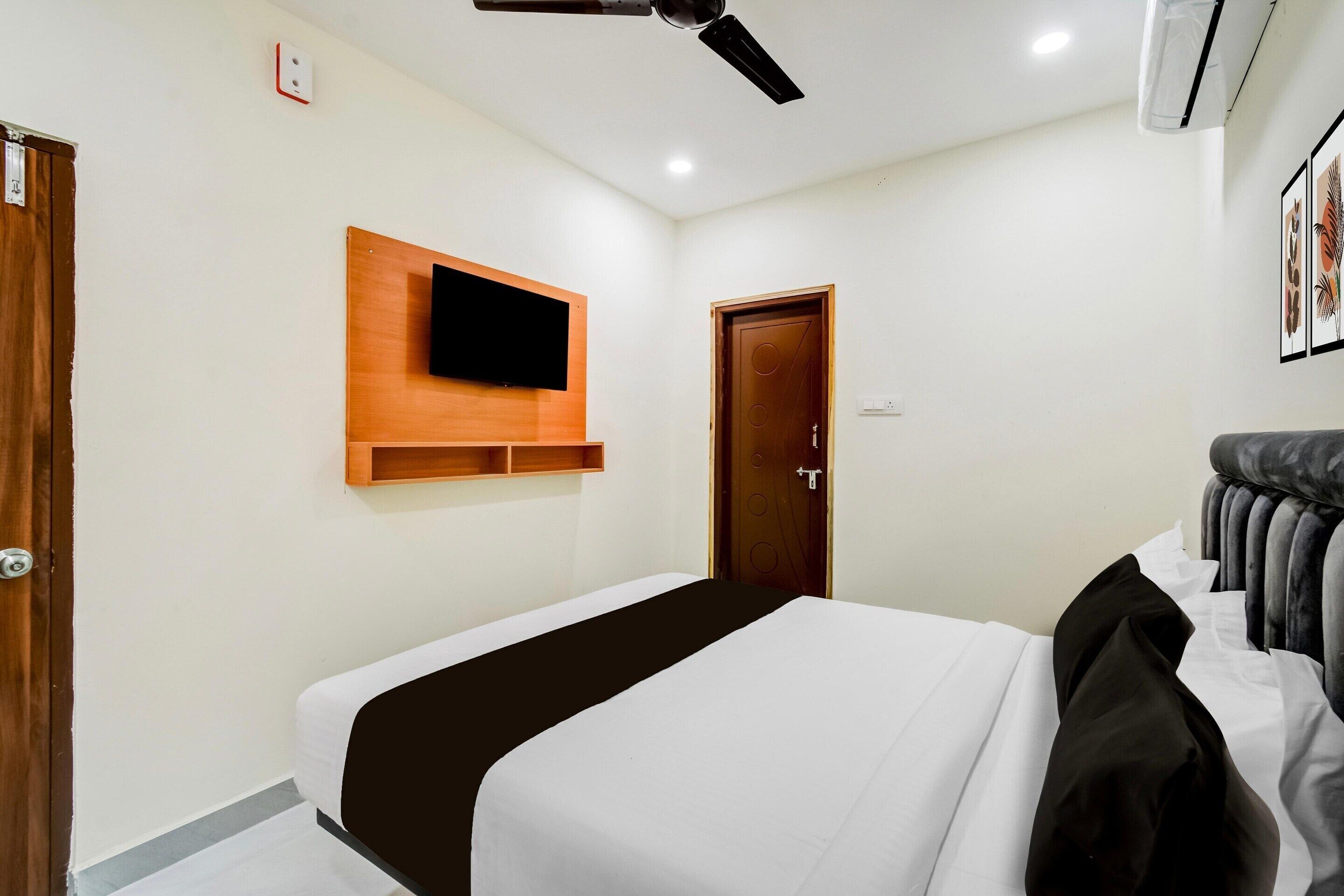 A hotel room with a bed, a mounted TV, a door, and a ceiling fan.