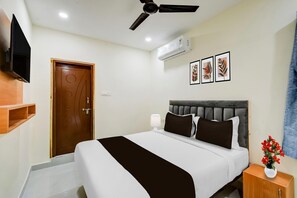 Ein Hotelzimmer mit einem Bett, einem Deckenventilator, einer Klimaanlage, einem an der Wand befestigten Fernseher und gerahmten Kunstwerken.