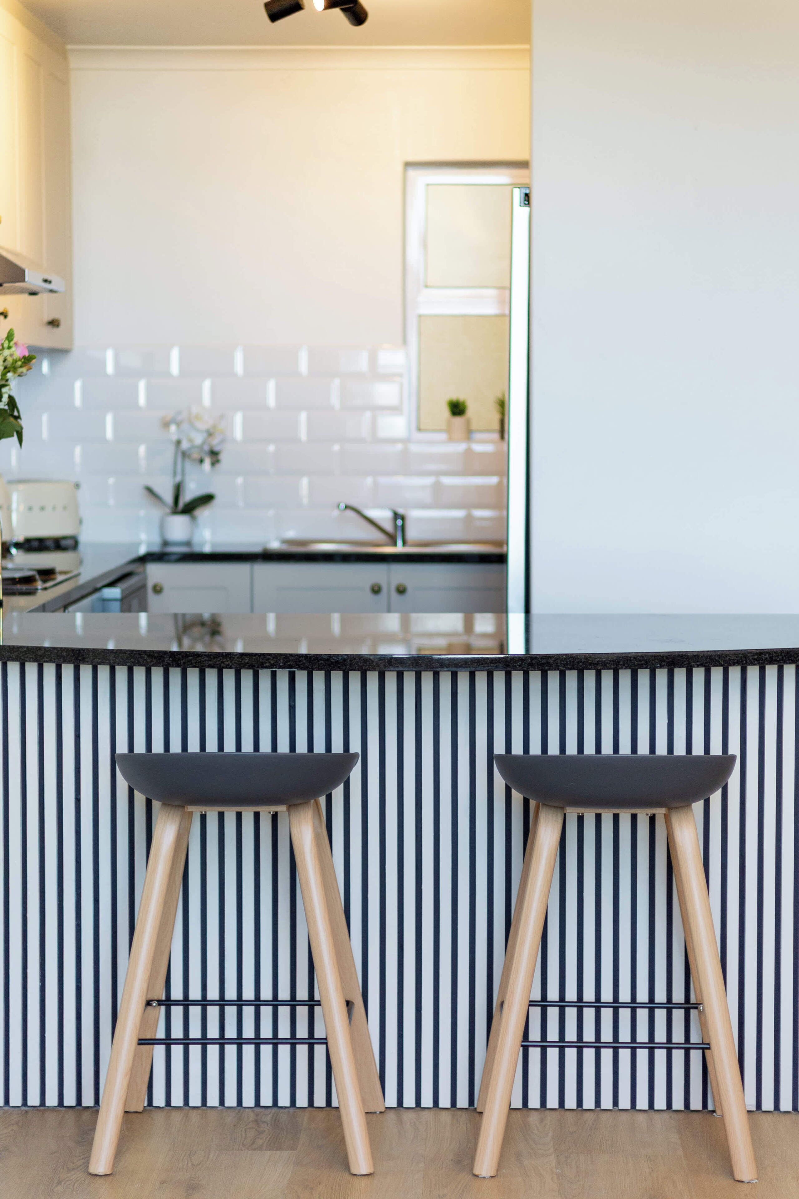 A modern kitchen with a black countertop, two wooden stools, and a striped backsplash.