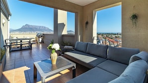 A spacious balcony with a sofa, a table, and a vase of flowers. - 2 Bedroom, Mountain View Penthouse, Century City (Cape Town)
