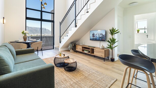 A spacious living area with a staircase, a sofa, a dining table, and a TV. - 2 Bedroom, Mountain View Penthouse, Century City (Cape Town)