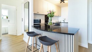 A modern kitchen with a black countertop, white cabinets, and two black bar stools. - 2 Bedroom, Mountain View Penthouse, Century City (Cape Town)