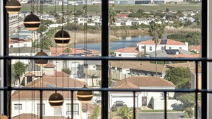 A view through a window with hanging spherical light fixtures, a distant mountain, and a residential area with houses and a body of water. - 2 Bedroom, Mountain View Penthouse, Century City (Cape Town)