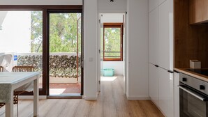 A modern kitchen with white cabinets, a wooden countertop, and a sliding glass door leading to a balcony.