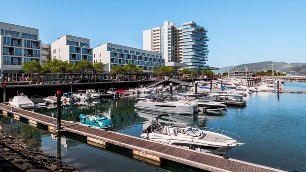 A marina with boats docked, a wooden pier, and modern buildings in the background.