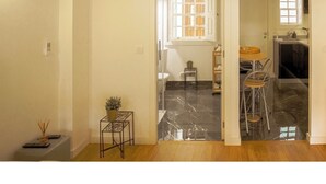 A spacious room with a wooden floor, a small table with chairs, and a window with a view of the outside. - Alojamento 5 Outubro (Amarante)