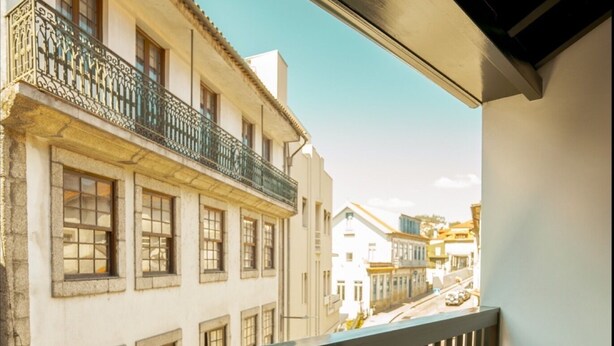 A balcony with a table and chairs, overlooking a street with buildings and pedestrians. - Alojamento 5 Outubro (Amarante)