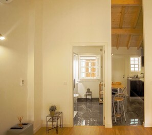 A spacious room with a wooden floor, a small table with chairs, and a window with a view of the outside. - Alojamento 5 Outubro (Amarante)