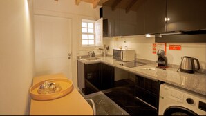 A compact kitchen with dark cabinets, a microwave, a coffee maker, and a washing machine. - Alojamento 5 Outubro (Amarante)