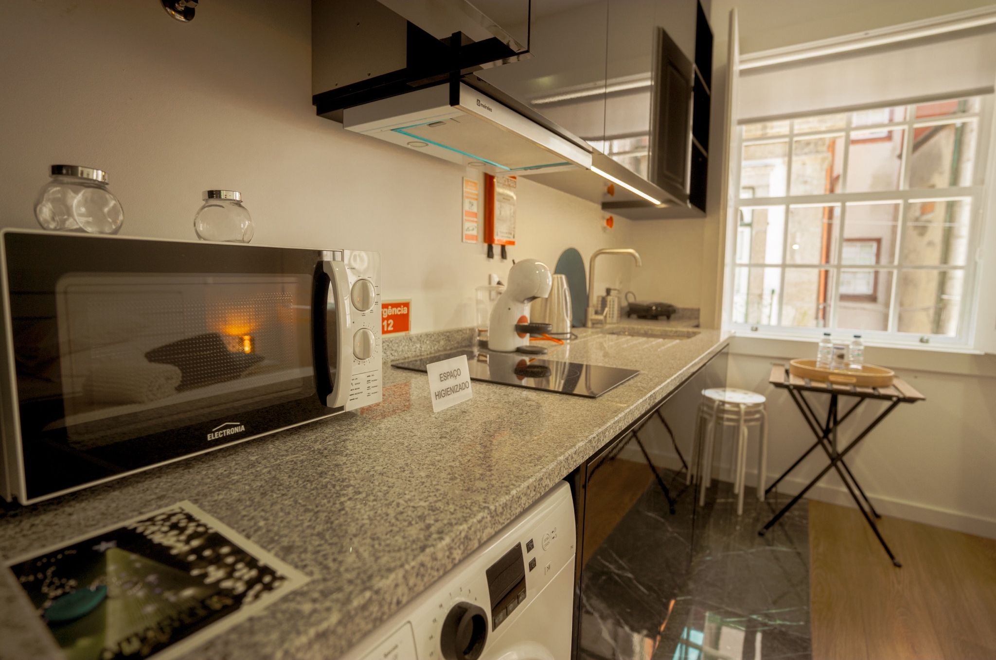 Eine moderne Küche mit Mikrowelle, Toaster und Kaffeemaschine. Ein Fenster bietet Blick ins Freie.