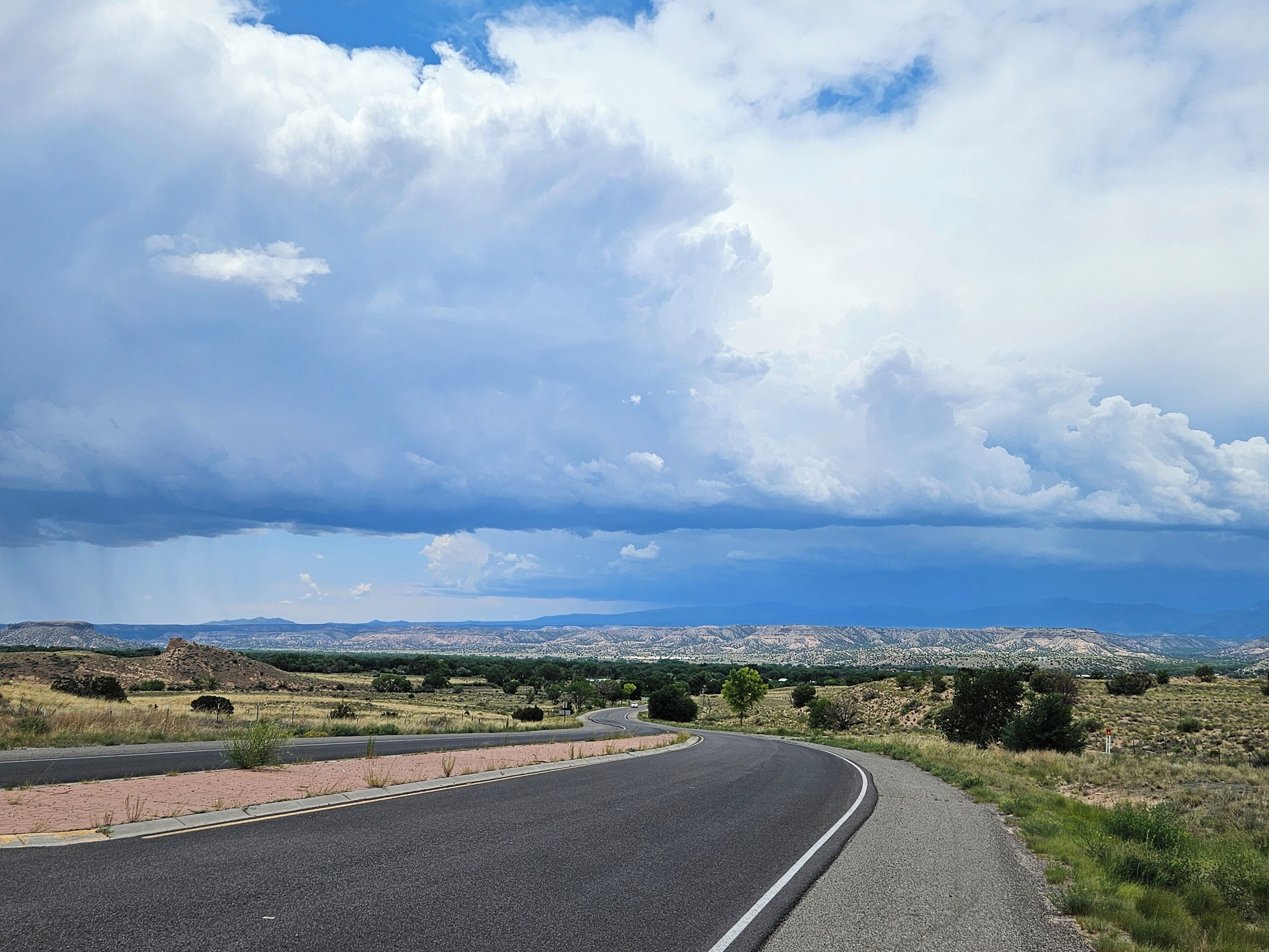 A curving road with a clear sky and distant cityscape.