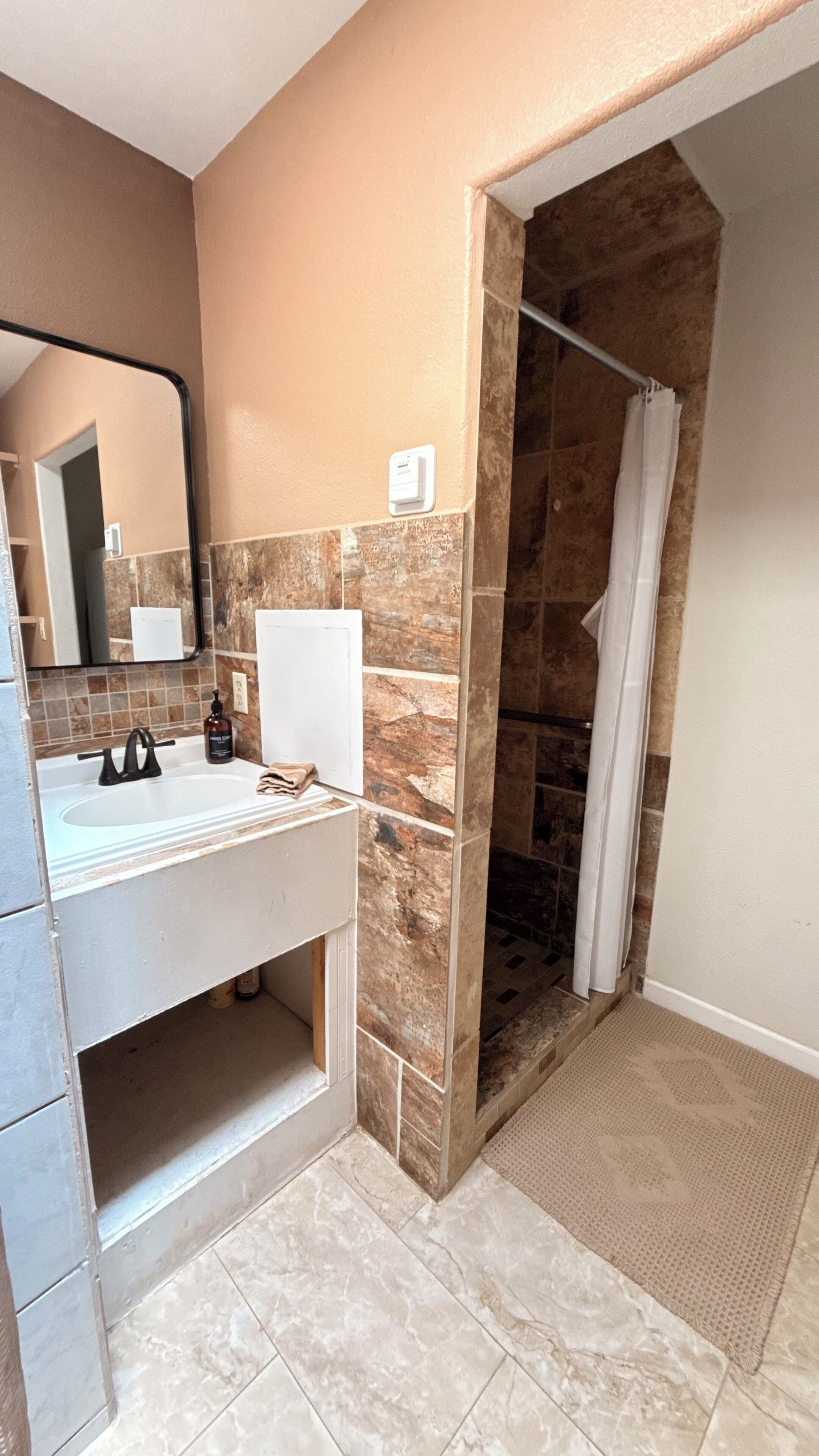 A bathroom with a white sink, a mirror, a shower with a glass door, and a tiled floor.
