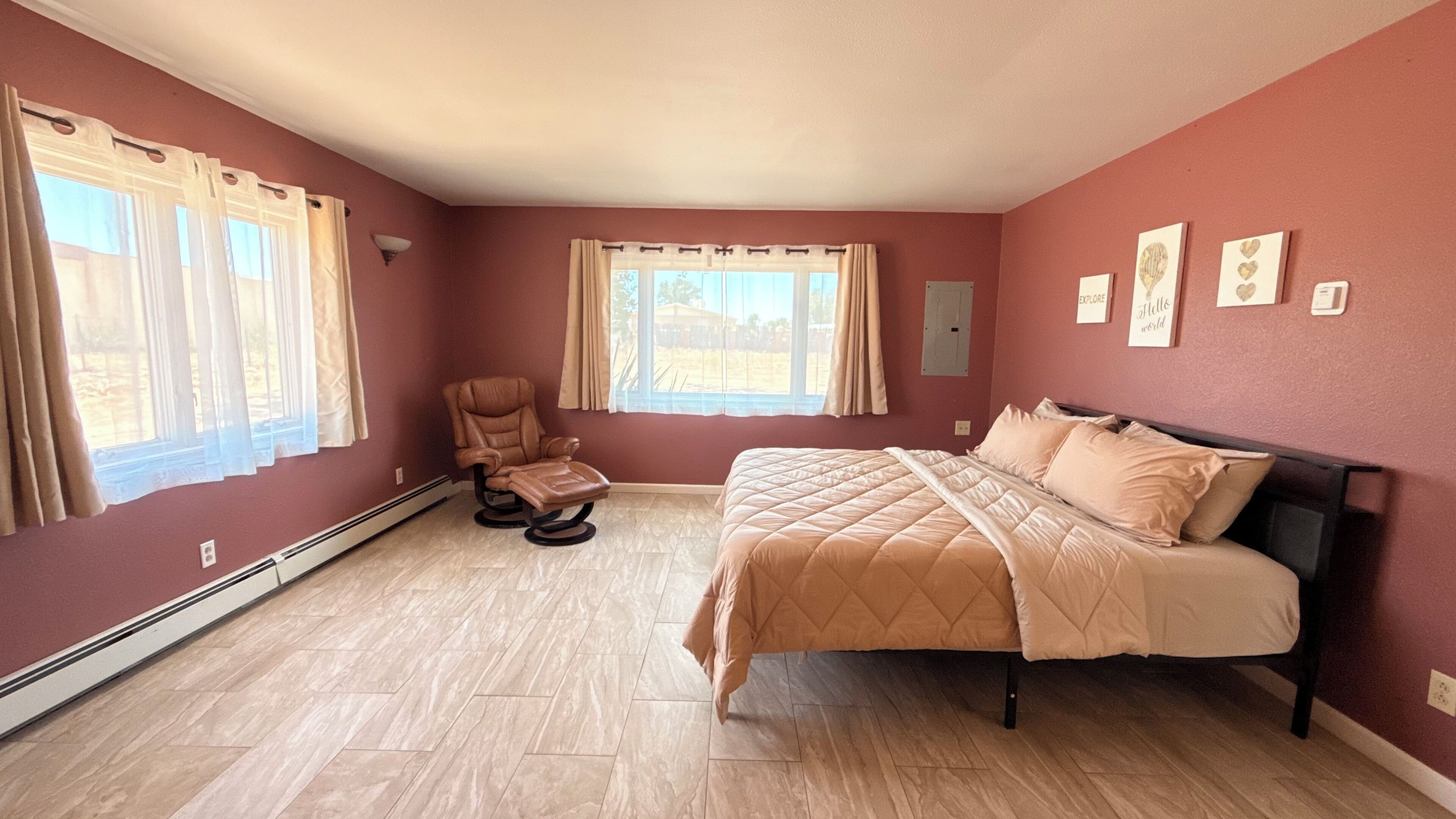 A bedroom with a bed, a massage chair, and two windows with curtains.