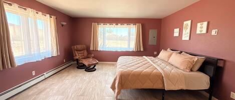 A bedroom with a bed, a massage chair, and two windows with curtains.
