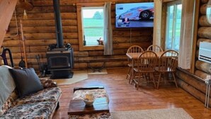 Ein rustikales Blockhaus-Interieur mit einer Couch, Sesseln, einem Kamin und einem Fernseher.