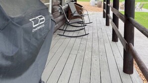 Eine Holzhütte mit Veranda, Grill und Schaukelstuhl.