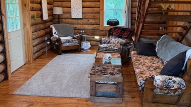 Ein Blockhaus-Interieur mit Holzboden, einer Couch, einem Sessel, einem kleinen Tisch und einem Fenster.