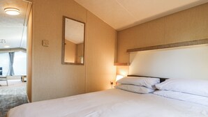 A hotel room with a bed, a bedside lamp, a mirror, and a window with curtains. - White Hart Caravan (Battle)
