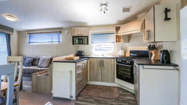 A compact RV kitchen with a microwave, stove, and sink. - White Hart Caravan (Battle)