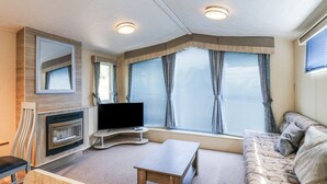 A compact living space with a sofa, a small table, a flat-screen TV, and a fireplace. - White Hart Caravan (Battle)