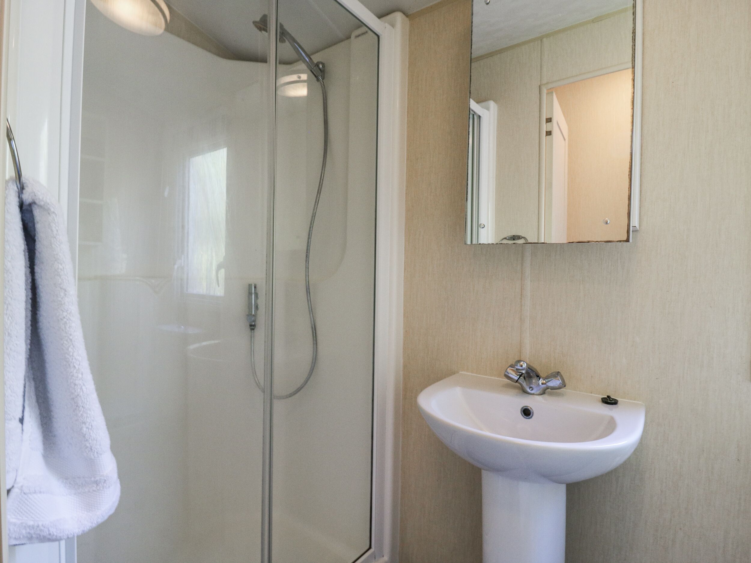 Un baño con ducha envuelta en vidrio, un lavabo blanco y un espejo encima.