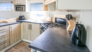 A compact kitchen with a microwave, stove, and knife block. - White Hart Caravan (Battle)