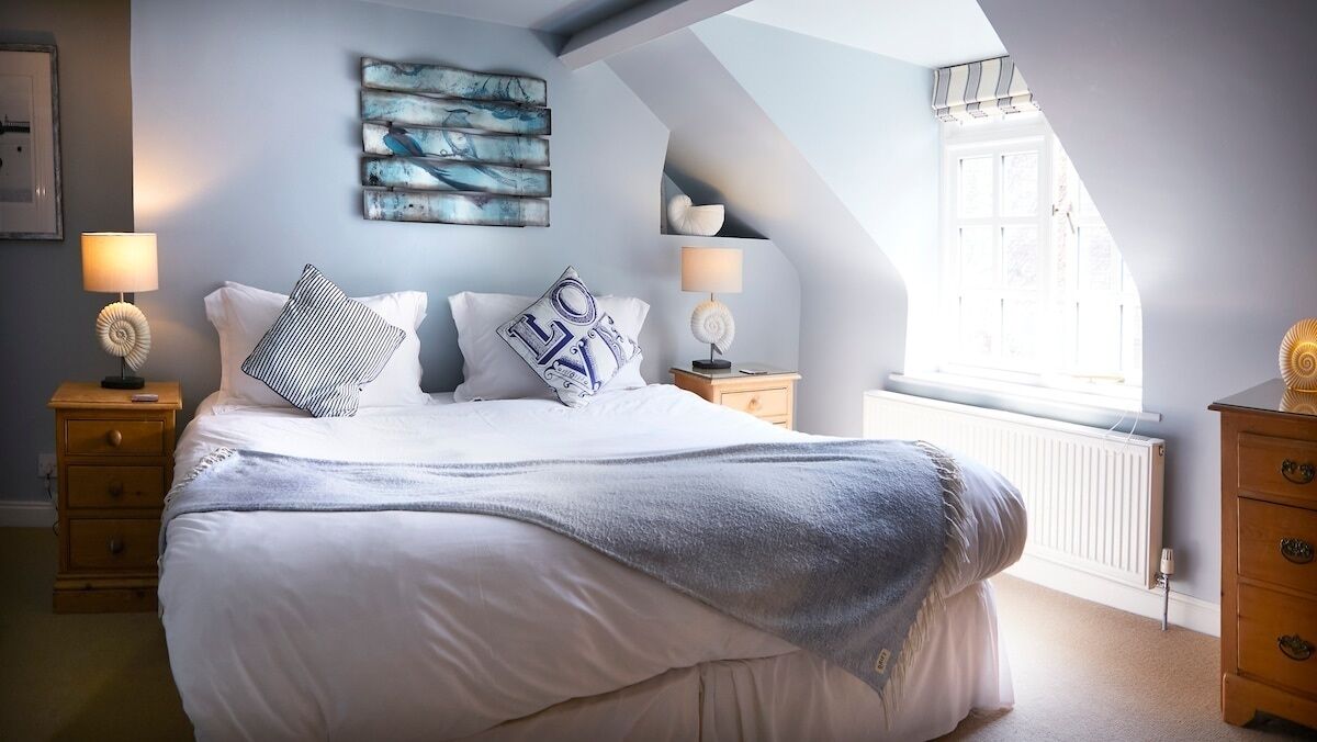 A bedroom with a large bed, two bedside tables with lamps, a window with a view, and a wall with artwork.