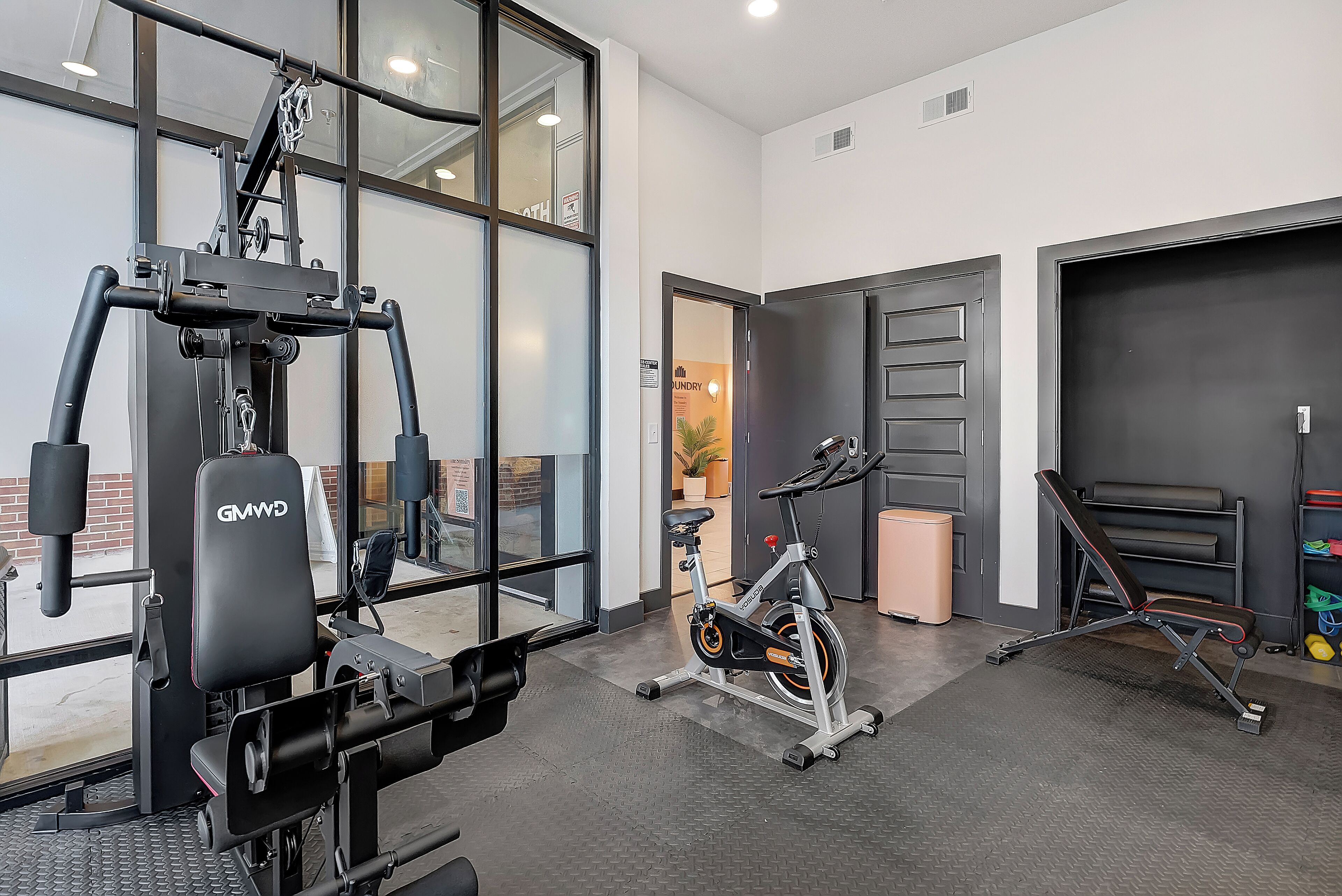 A gym with exercise equipment, a bench, and a door leading to a laundry area.