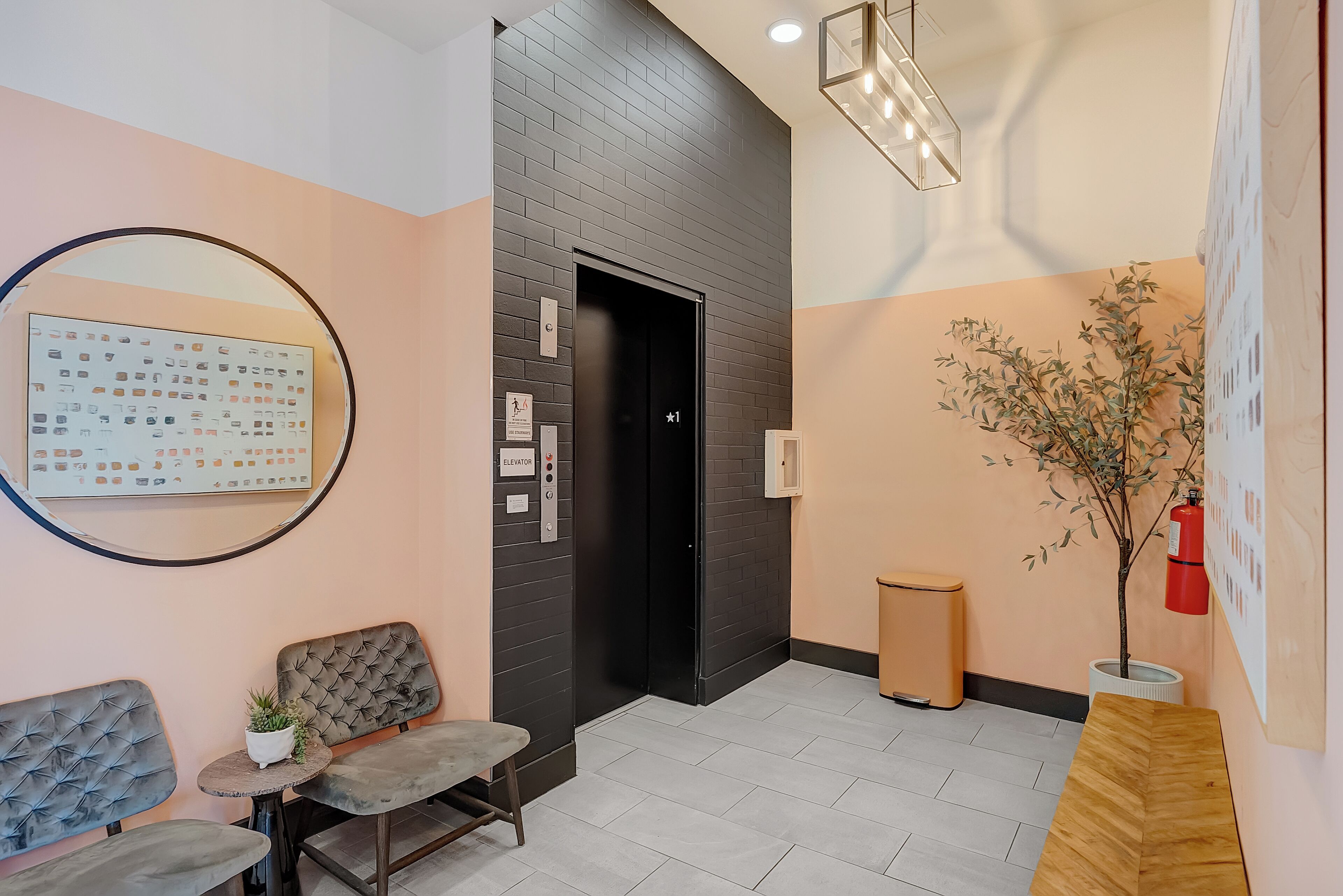 Een receptiezone met een zwarte lift, een wachtbank, een klein tafeltje met een plant en een brandblusser aan de muur.