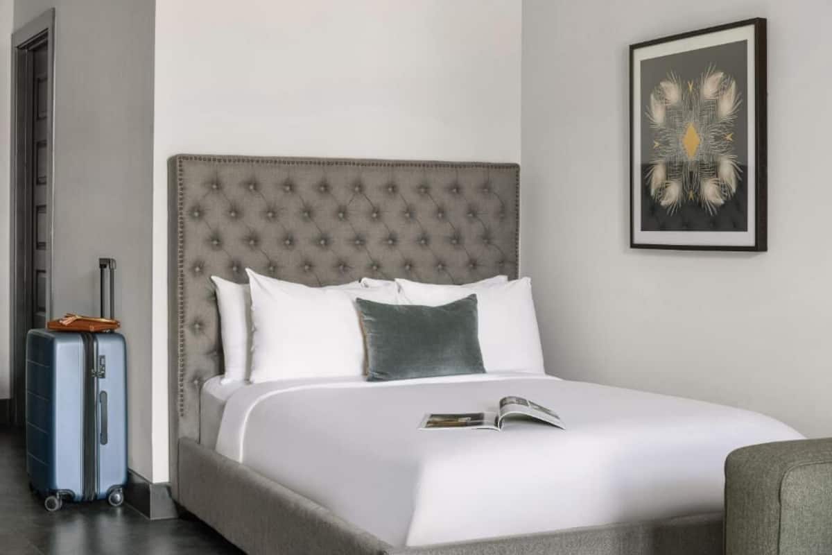 A neatly made bed with a tufted headboard, a suitcase, and a framed artwork on the wall.