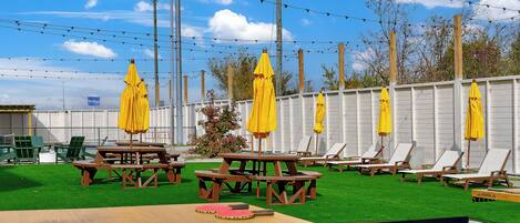 A patio area with wooden picnic tables and yellow umbrellas, surrounded by a white fence.