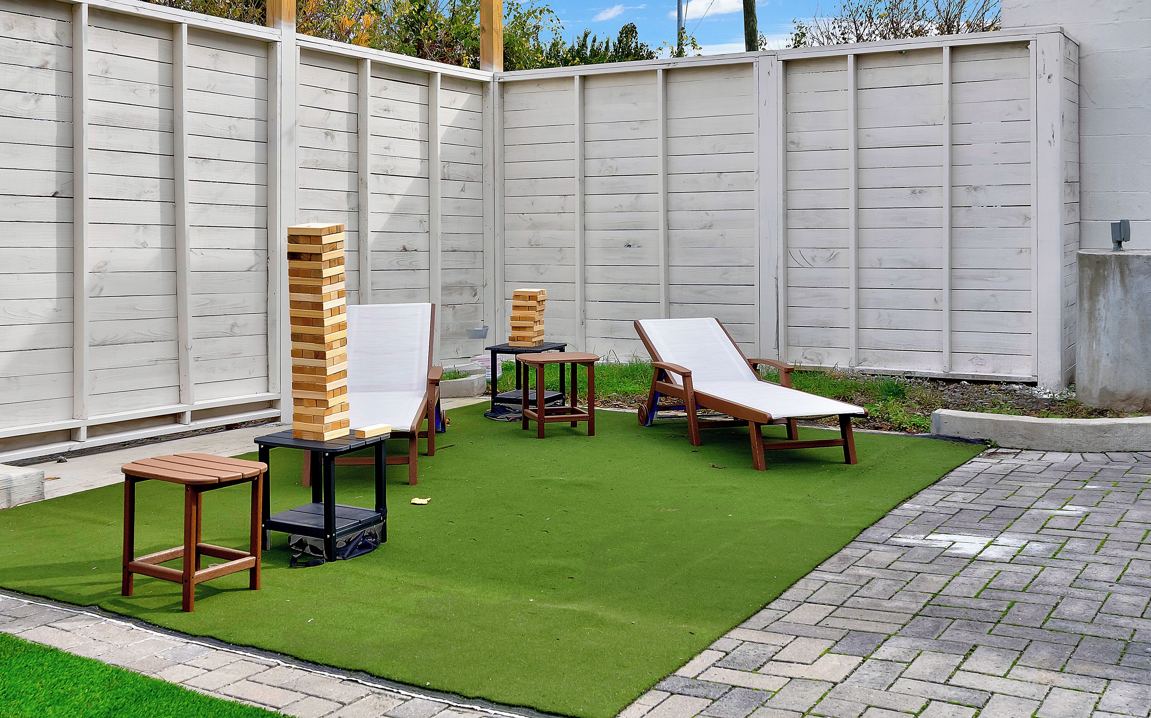 A patio with artificial grass, wooden furniture, and a white fence.