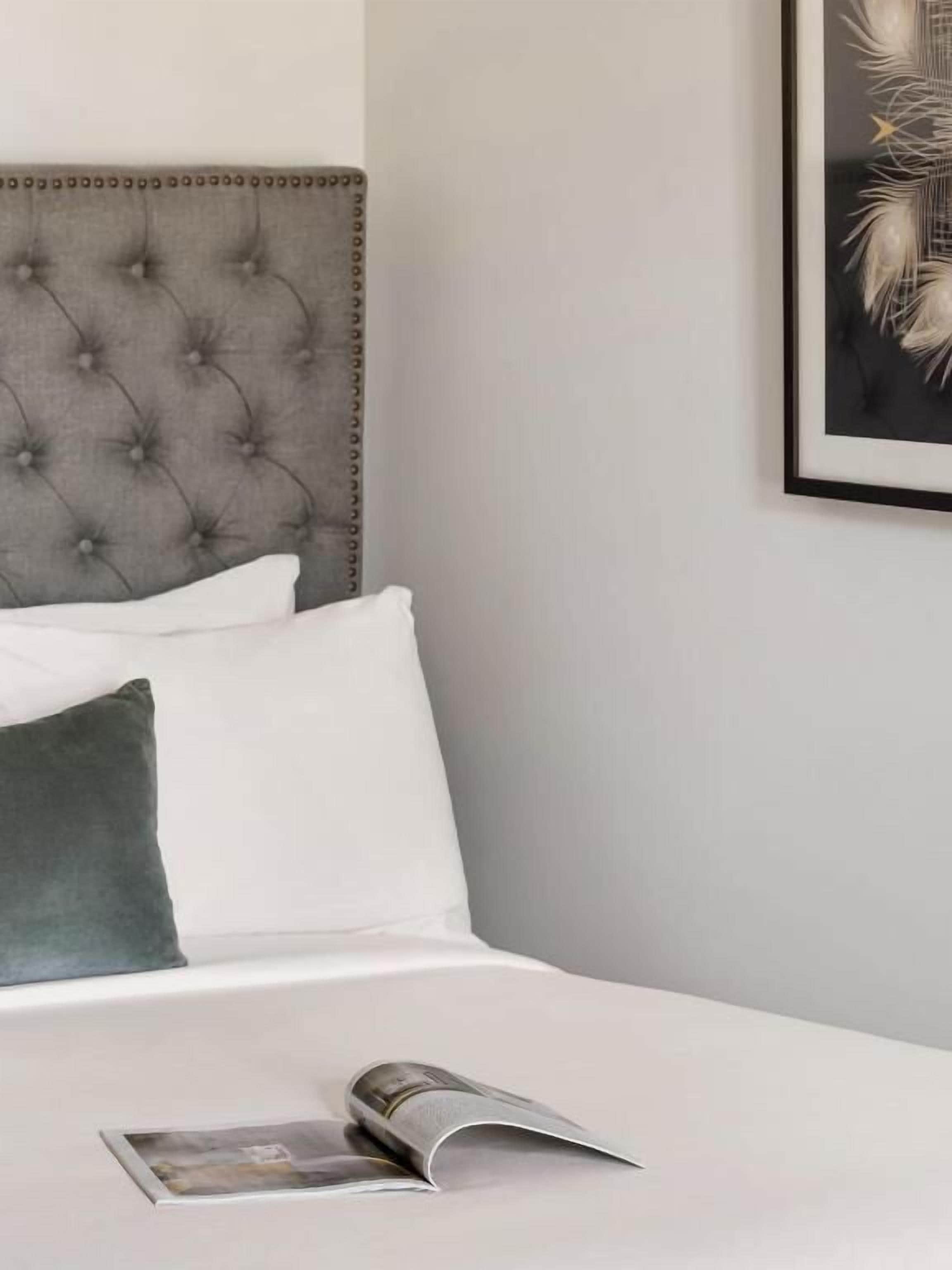 Una cama bien hecha con cabecera capitonada, almohadas blancas y verdes, y una revista sobre la cama.